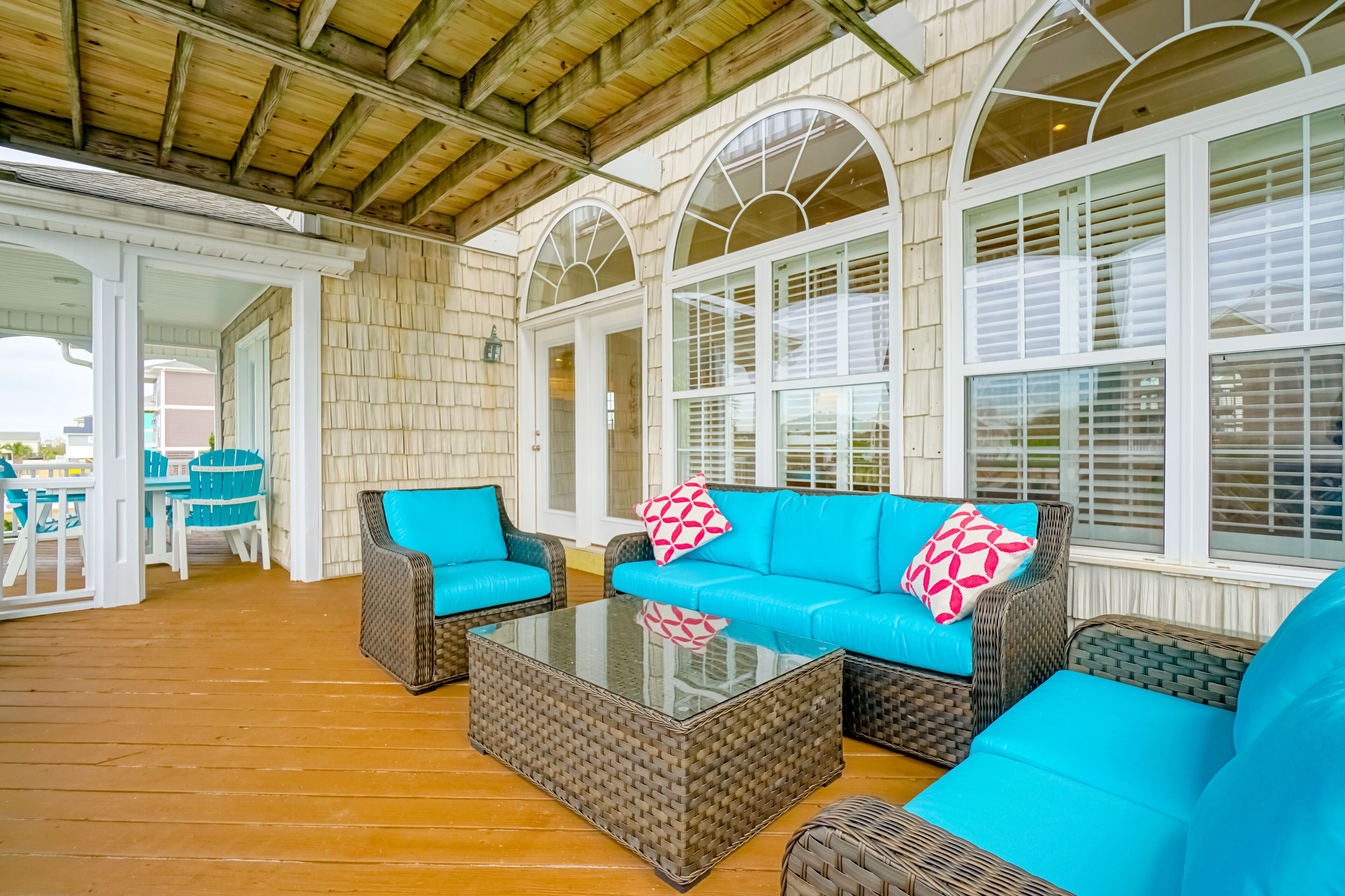 A covered outdoor seating area with wicker furniture and a glass-top coffee table.