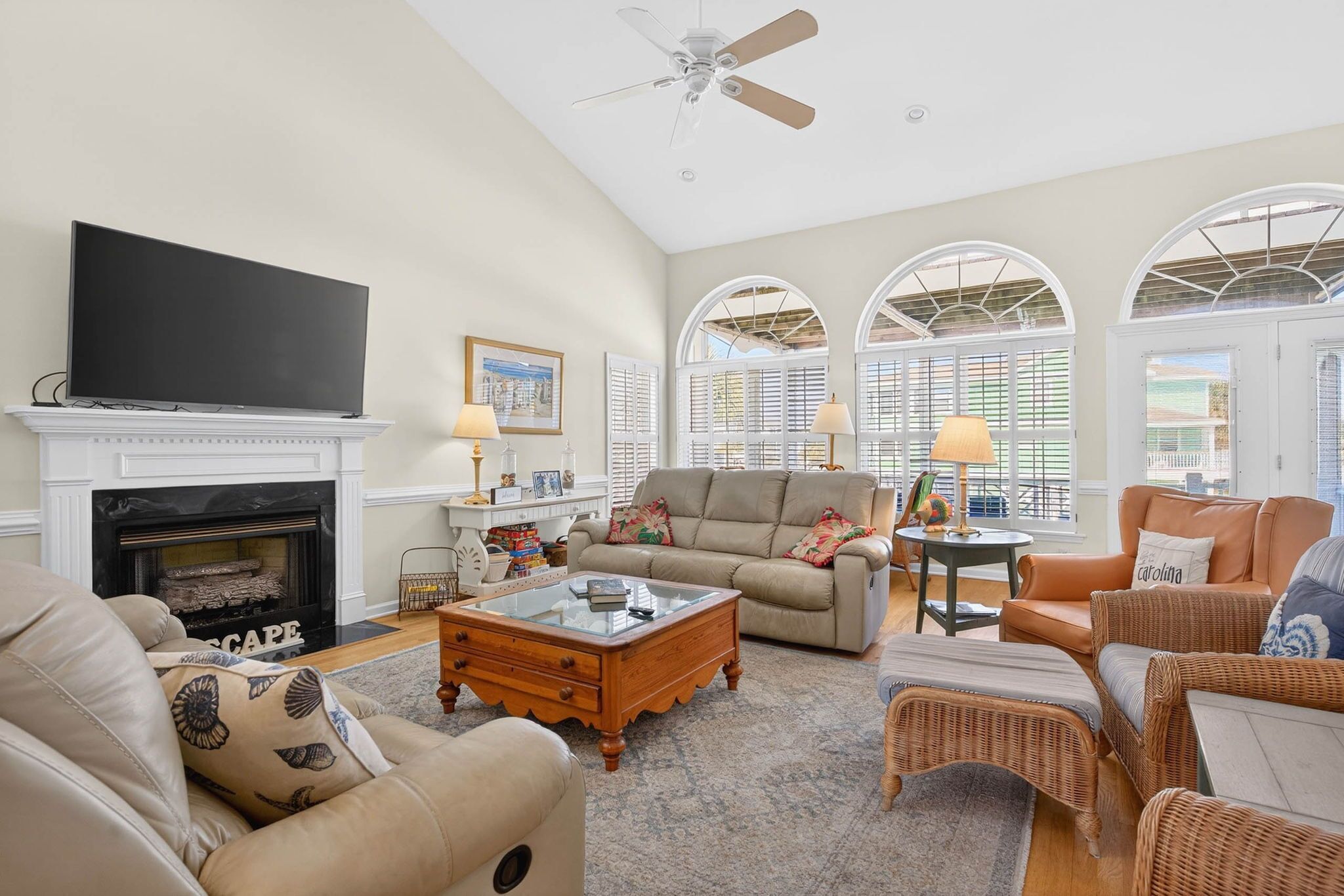 A spacious living room with a fireplace, comfortable seating, a television, and large windows.