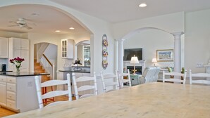 A spacious kitchen with white cabinetry, a marble island, and a dining area with a large table and chairs.