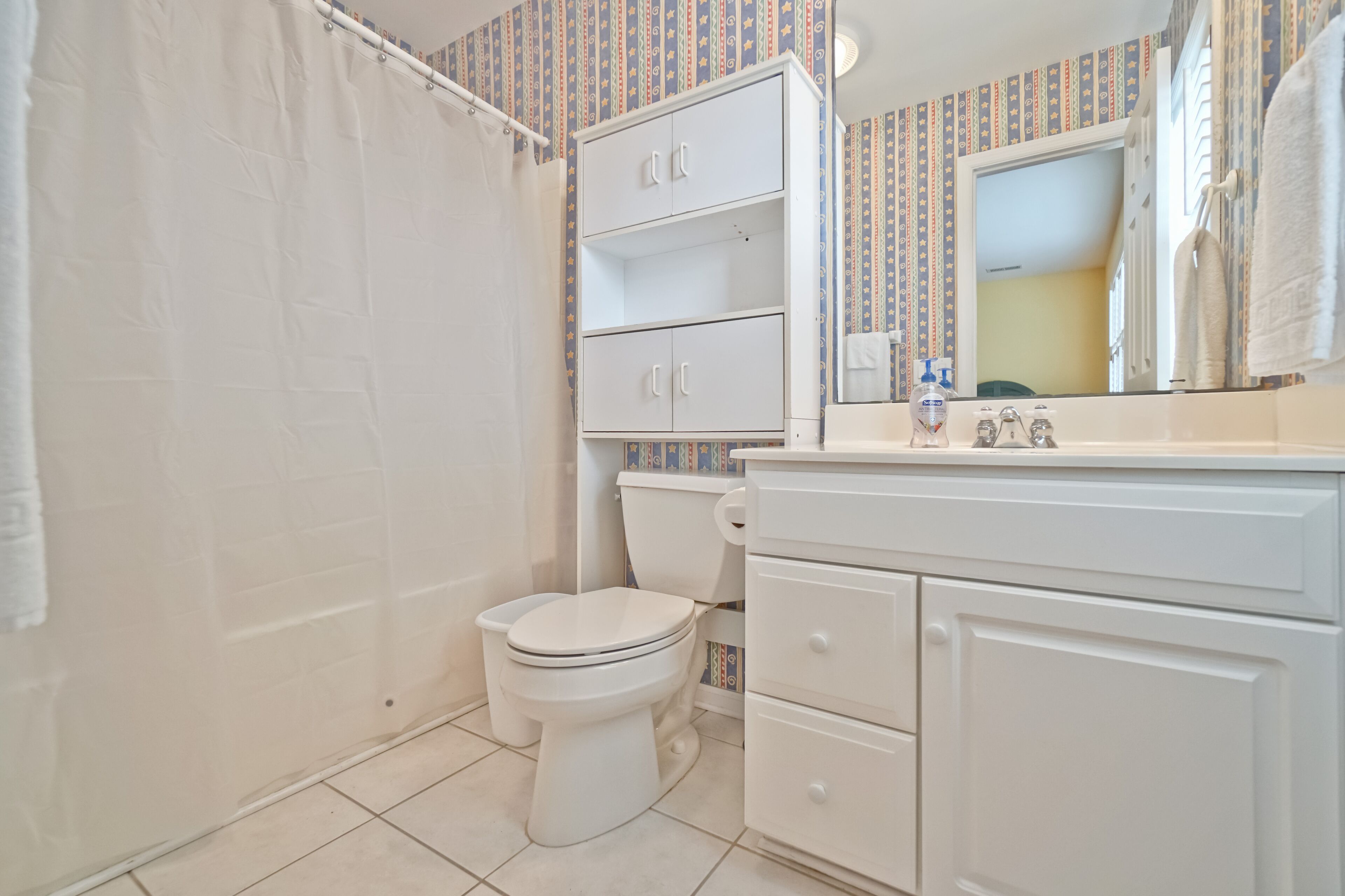 A bathroom with a toilet, a shower curtain, a sink with a mirror, and a cabinet.