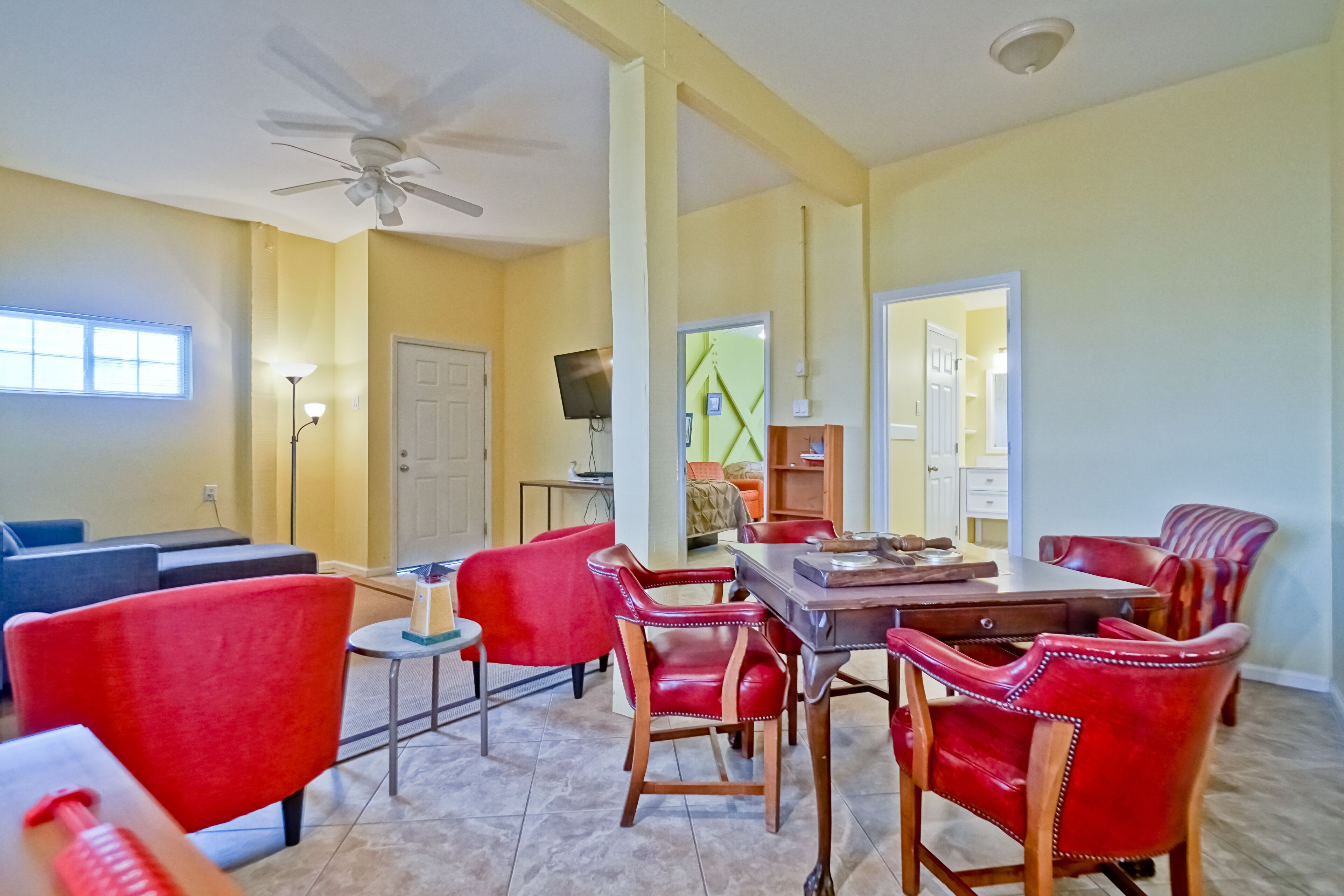 A dining area with a table and red chairs, a ceiling fan, and a TV on the wall.
