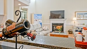 A kitchen counter with a wine rack, a fireplace, and a living room in the background.