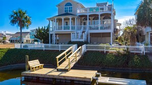 A large, two-story house with a balcony and a dock extending into a body of water.