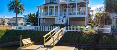 A large, two-story house with a balcony and a dock extending into a body of water.