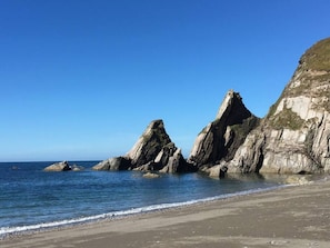 A coastal beach with rocky formations and clear blue skies.