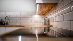 Una cocina con paredes de azulejos blancos, encimera de madera y electrodoméstico de acero inoxidable.