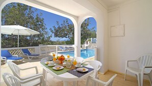 A sunlit outdoor dining area with a pool view, white furniture, and a table set with fruits and beverages. - Stunning private villa for 6 people with A/C, private pool, WIFI, TV and terrace (Vale Da Ursa)