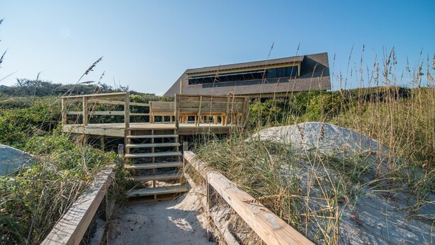 A modern beach house with a wooden deck and stairs leading to a large window overlooking the beach. - Ocean Breezes Historic Home with Creek Dock (Pawleys Island)