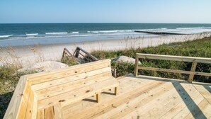 A wooden deck with a bench overlooking a beach with waves and a clear sky. - Ocean Breezes Historic Home with Creek Dock (Pawleys Island)