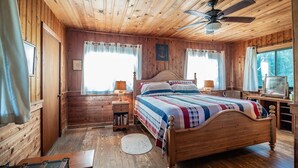 A wooden cabin bedroom with a bed, a ceiling fan, and a television. - Ocean Breezes Historic Home with Creek Dock (Pawleys Island)