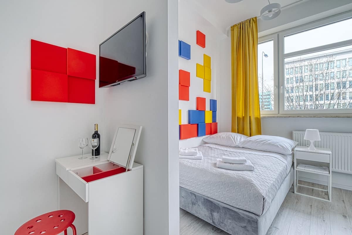 Quarto de hotel moderno com cama, escrivaninha e televisão de tela plana, além de um detalhe decorativo na parede.