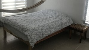 Une chambre à coucher comprenant un lit, un banc en bois, une fenêtre avec des stores et un appareil de climatisation.