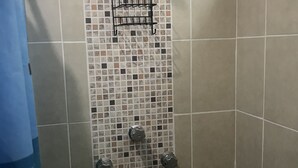 Une douche avec un mur carrelé, une étagère en métal et un pommeau de douche.