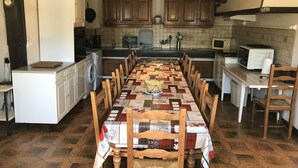 Une cuisine avec une longue table à manger, des chaises en bois, un lave-linge et un four à micro-ondes.