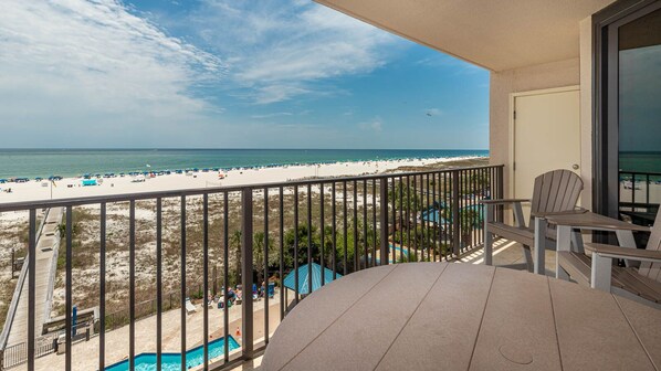 A balcony with a view of a beach, a pool, and a chair.