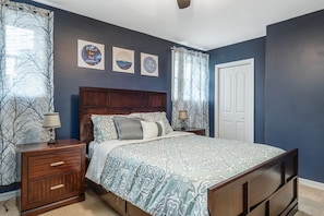 Un dormitorio con cama, mesitas de noche, un aparador de madera y una puerta.