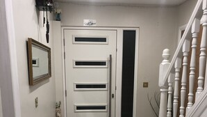 Ein Flur mit einer weißen Tür, einem kleinen Spiegel, einer Vase mit Blumen und einer Treppe mit weißen Pfosten.