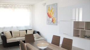 A modern living room with a sofa, dining table, and chairs. There is a painting on the wall and a cabinet with shelves. - Bella casa vacanze in Sardegna (Lotzorai)