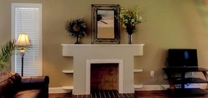 A living room with a fireplace, a couch, a TV stand, and a lamp.