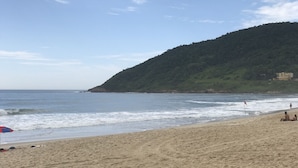 A beach with a sandy shore, waves, and a hill with greenery. - House with 2 bedrooms in a condominium. (Praia da Gamboa)