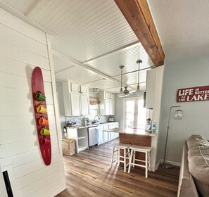 Cucina con mobili bianchi, soffitto in legno e decorazione con una tavola da surf rossa.