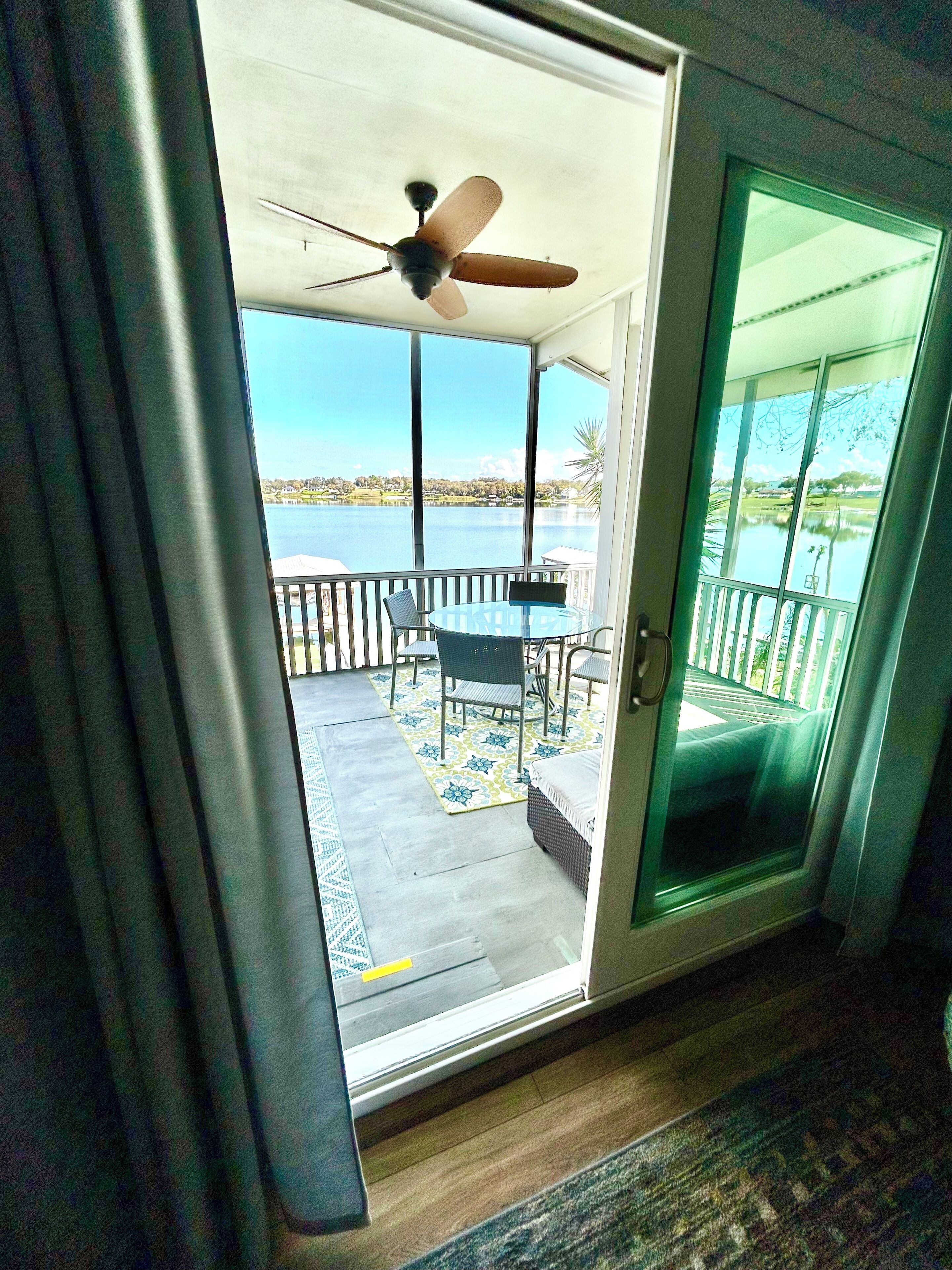 Une pièce dotée d’une porte-fenêtre coulissante donnant sur un balcon extérieur équipé d’une table, de chaises et d’un ventilateur de plafond.