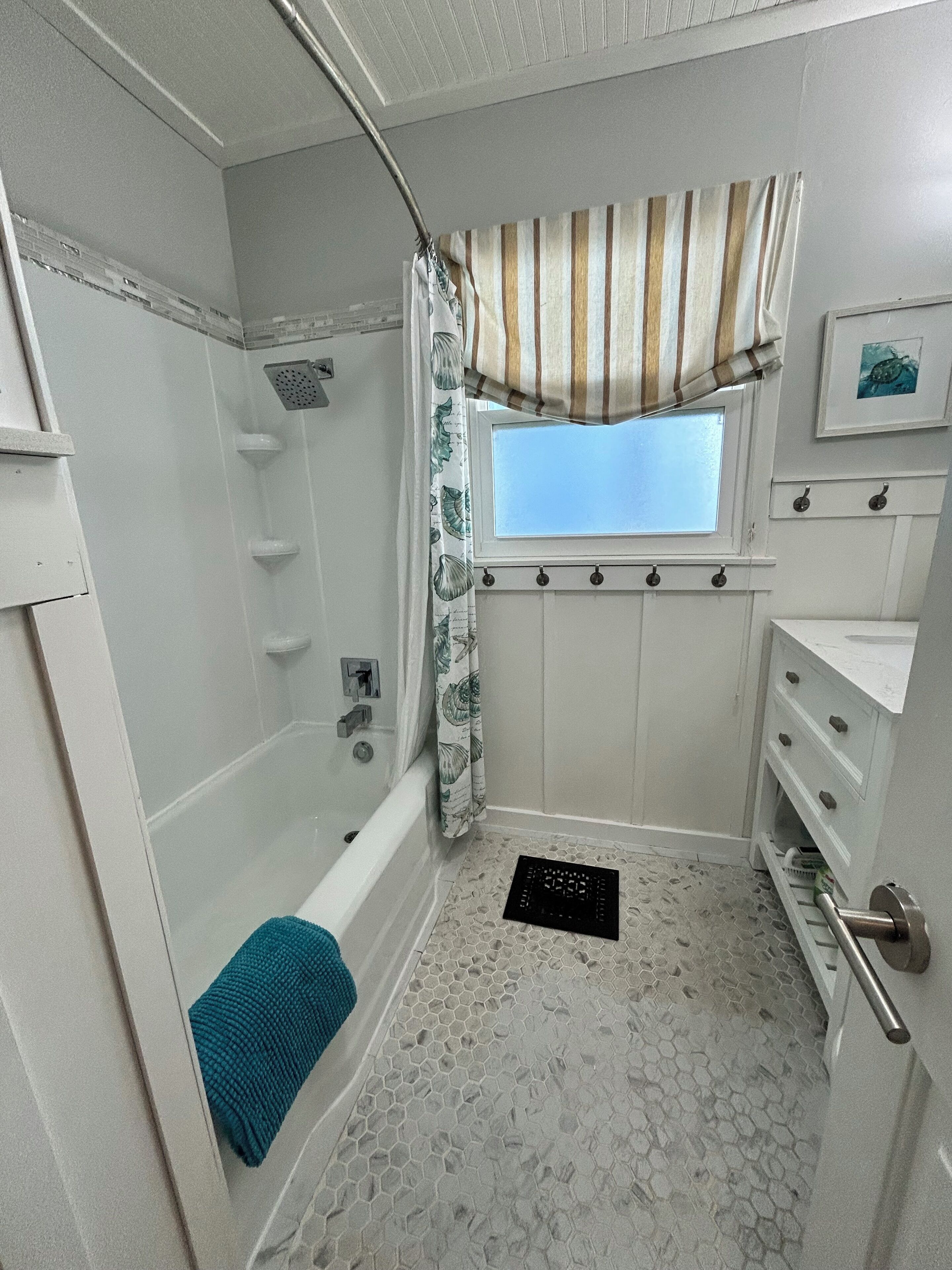 A bathroom with a shower, a window, a sink, and a towel rack.