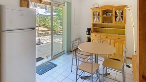 Une cuisine avec un réfrigérateur blanc, un meuble en bois doté de portes en verre, une table à manger avec quatre chaises et une grande fenêtre donnant sur un paysage verdoyant.