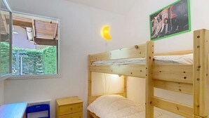 Une chambre avec un lit superposé, un bureau, une chaise et une petite commode.