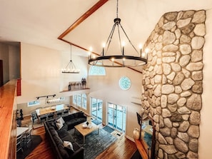 A spacious living area with a stone wall, a chandelier, and a dining area with a wooden table and chairs. - THE LIGHTSHIP ON MOOSE POND & PLEASANT MOUNTAIN - Sleeps 30! (Bridgton)