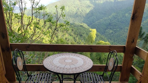 Una terraza de madera con una mesa redonda y dos sillas, con vistas a un paisaje montañoso.