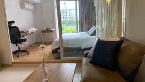 A hotel room with a bed, a sofa, a desk with a chair, and a window with curtains. - Hua Hin Condo 200m near beach (Nong Kae)