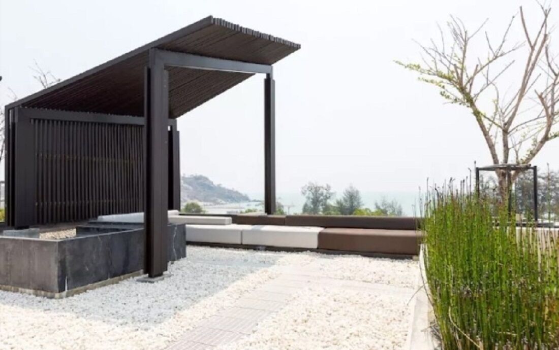 Un área de estar exterior moderna con una pérgola, una jardinera de concreto y vistas al mar.