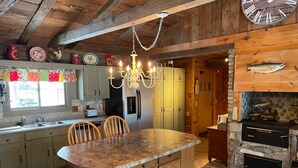A rustic kitchen with a central island, wooden cabinets, a stone fireplace, and a hanging chandelier. - Beautiful Cabin with Gorgeous Riverbend View. Great for relaxation and fishing! (Branch Township)