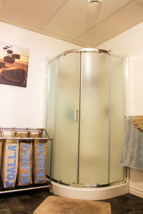 Une salle de bain avec une douche à parois de verre, un porte-serviettes avec une serviette, et une étagère contenant des sacs étiquetés « ORLLO BLANCO ».