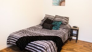Ein ordentlich gemachtes Bett mit gestreifter Bettwäsche, ein kleiner Nachttisch und ein an der Wand befestigtes Kunstwerk.