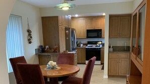 A dining area with a round table and four chairs, a kitchen in the background, and a wooden cabinet to the right. - Tranquil 3BR, 2BA Condo at Indian Palms - near Coachella (Indio)