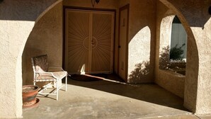 A covered patio area with a large wooden door, a chair, and a potted plant. - Tranquil 3BR, 2BA Condo at Indian Palms - near Coachella (Indio)