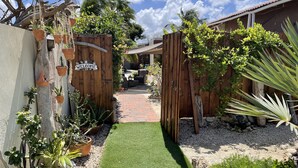 A garden pathway leading to a wooden gate with a 'WELCOME' sign, surrounded by potted plants and a small lawn. - Excellent place for heavenly peace with gardens and a relaxt swimmingpool (Noord)