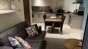 A modern living room with a leather sofa, a wooden dining table, and a kitchen in the background. - Excellent place for heavenly peace with gardens and a relaxt swimmingpool (Noord)