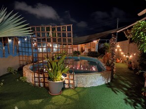 A pool surrounded by a wooden fence, potted plants, and string lights.