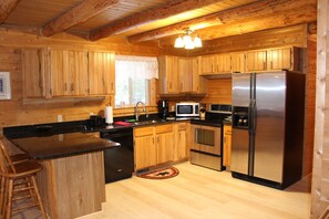 Interior de una cabaña de madera con cocina, que incluye armarios de madera, un refrigerador de acero inoxidable, un microondas y un lavabo.