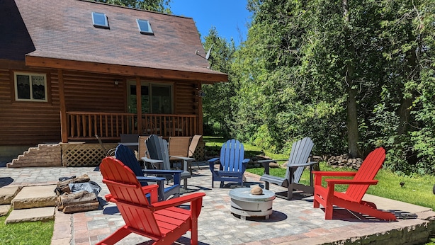 Een houten hut met een terras, voorzien van Adirondack-stoelen en een vuurkuil.