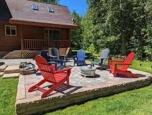 Una cabaña de madera con un patio que tiene sillas Adirondack y un hogar para fogata.