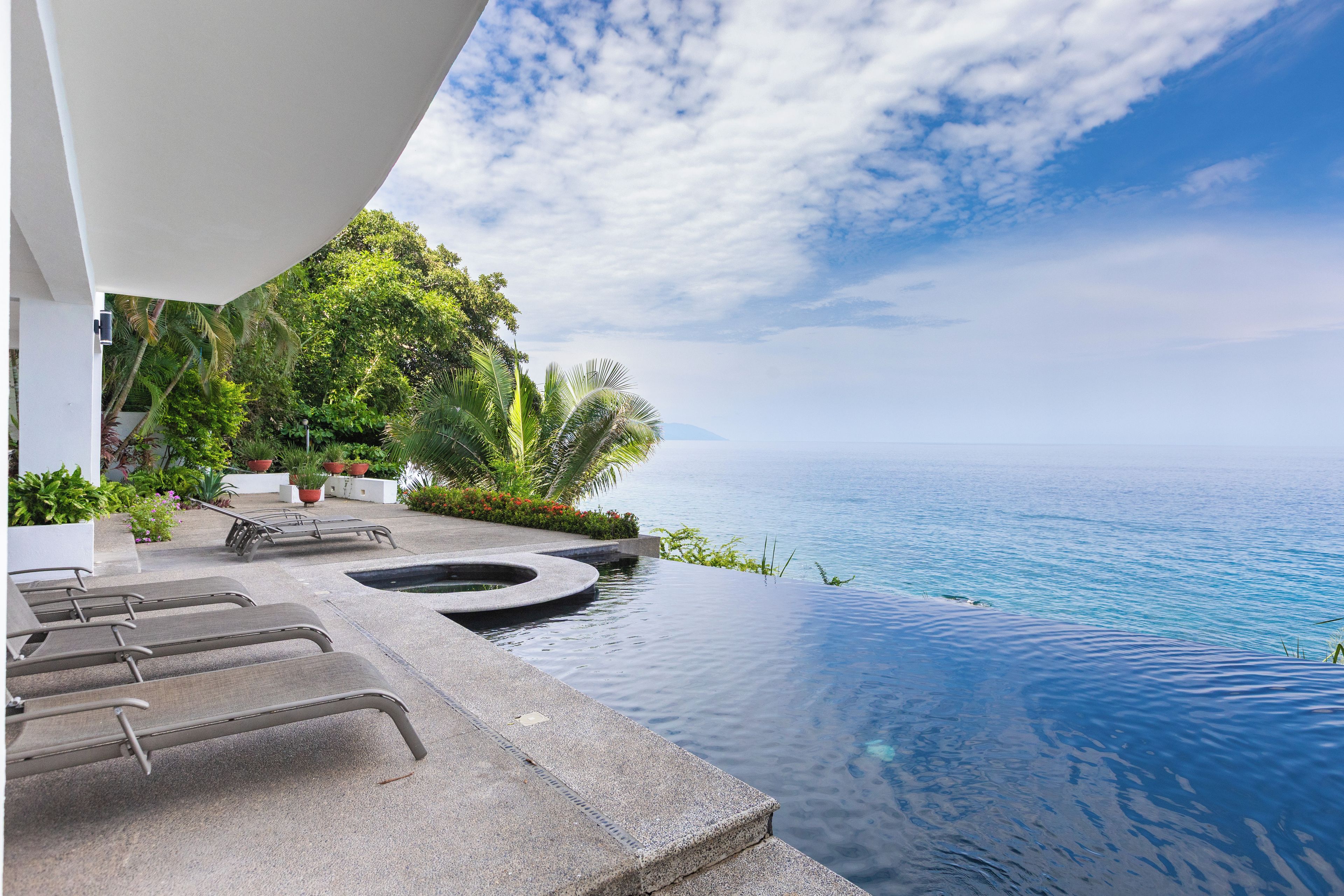 A infinity pool with a view of the ocean, lounge chairs, and potted plants.