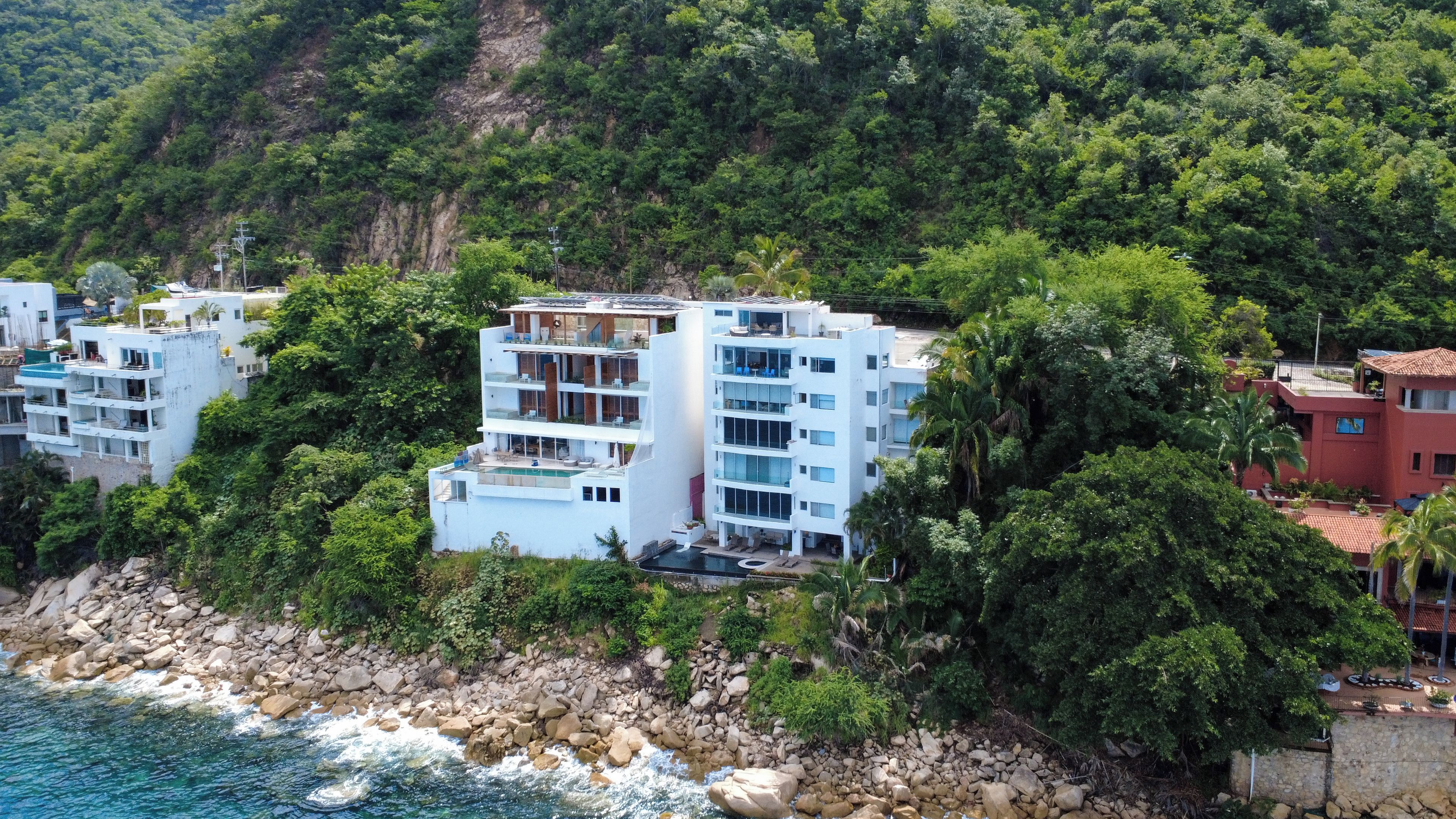 Un ensemble de bâtiments situé sur la côte, comprenant plusieurs étages, des balcons et un espace piscine.