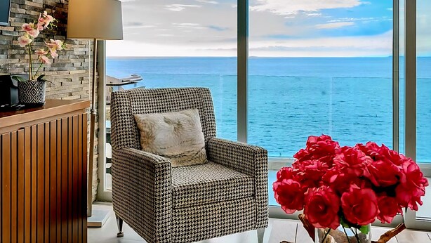 A high-rise room with a large window overlooking the sea, a patterned armchair, a lamp, and a vase of red flowers. - Exclusive Penthouse Oceanfront, small Condominium complex (Conchas Chinas)