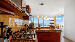 A modern kitchen with a large island, stainless steel appliances, and a view of the ocean. - Exclusive Penthouse Oceanfront, small Condominium complex (Conchas Chinas)