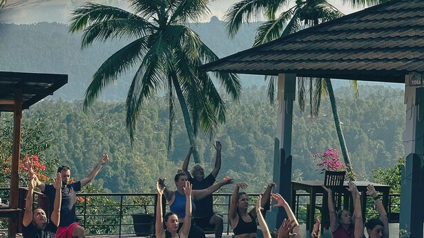 Clase de yoga al aire libre con piscina y paisaje tropical de fondo.