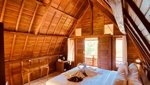 Un dormitorio acogedor en el ático, con techo de madera, una cama con ropa de cama blanca y un escritorio con silla.